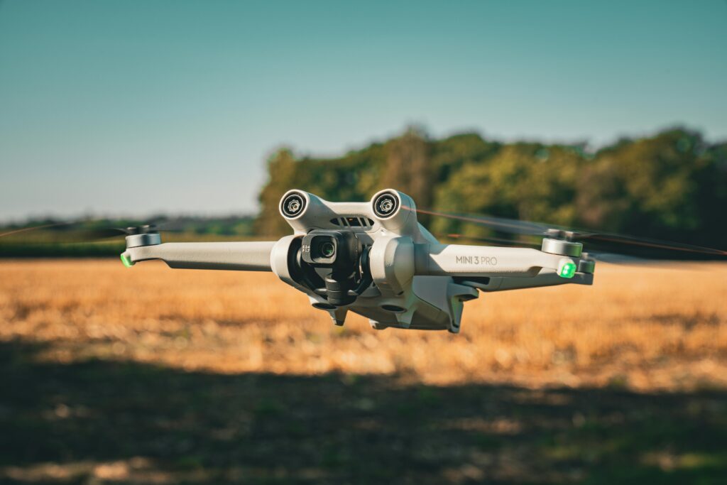 A DJI Mini 3 Pro drone flying over an open field with a clear, blue sky backdrop.
